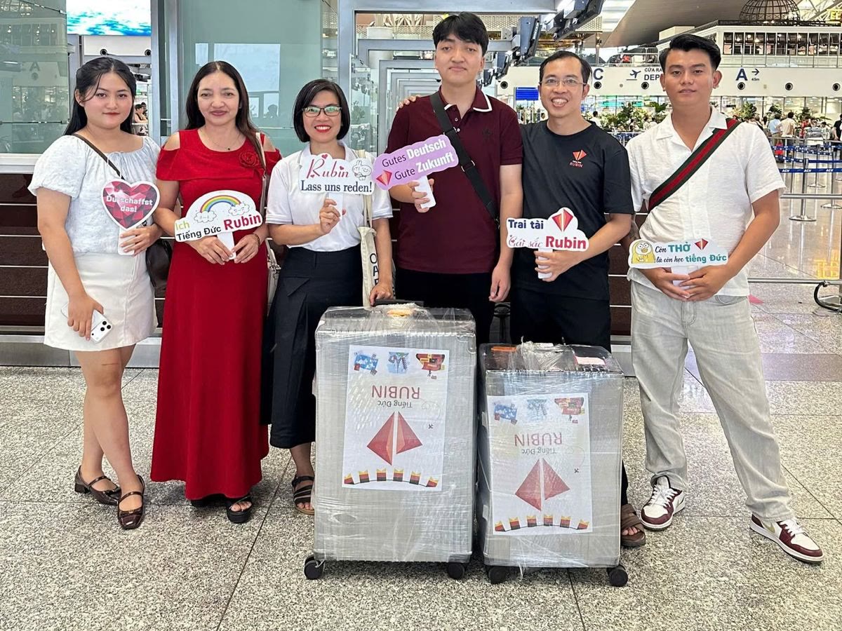 Ein Auszubildender mit zwei Koffern, verabschiedet von fünf Begleitern in der Abflughalle des Flughafens Hanoi.